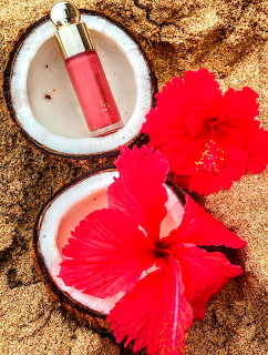 Halved coconut with pink bottle inside and two red hibiscus flowers on sandy beach