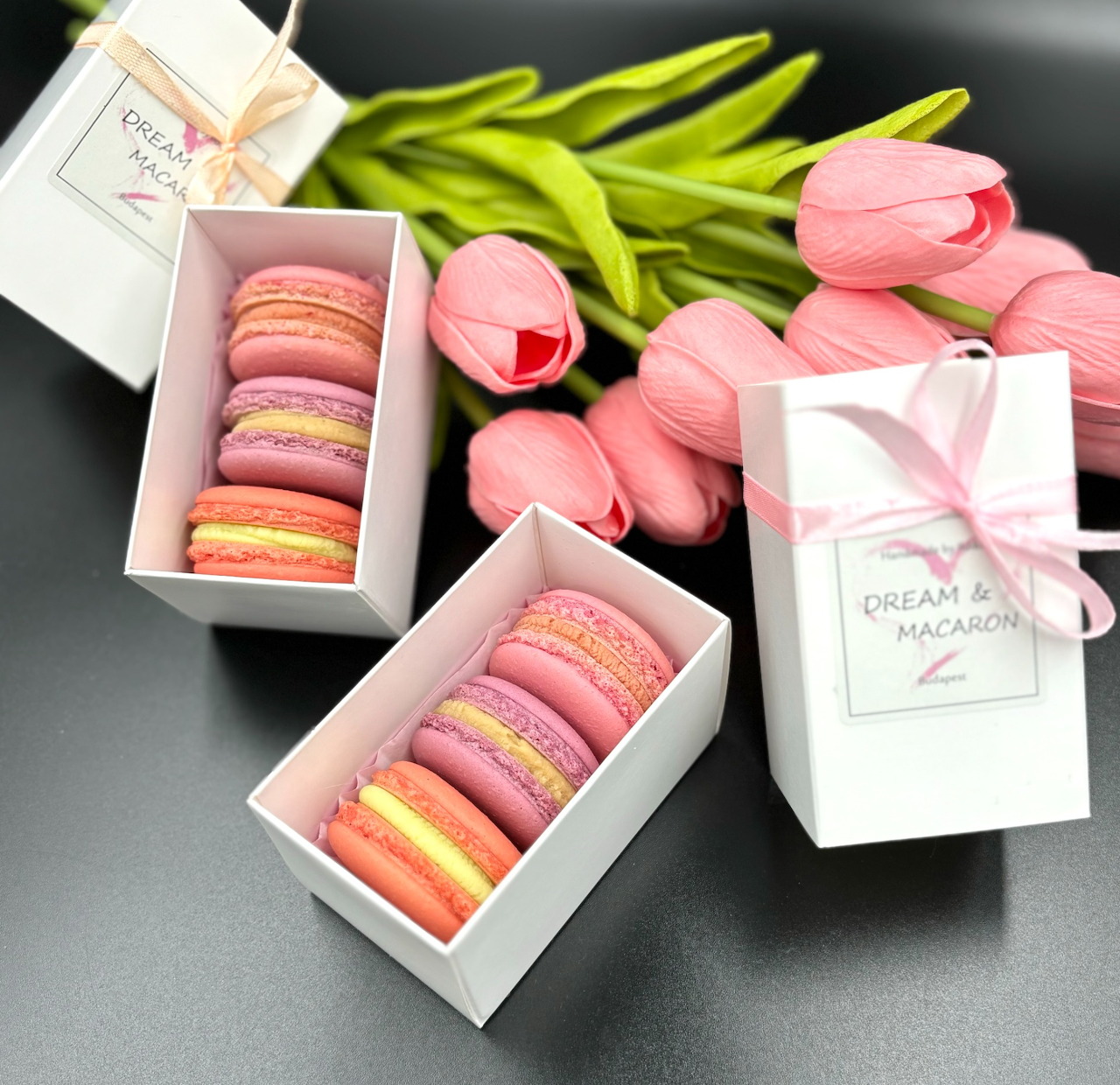 Pink macarons in white boxes with pink tulips on dark background
