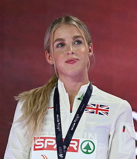 Young British female athlete with a medal around her neck wearing a white SPAR-branded jacket at an athletics ceremony