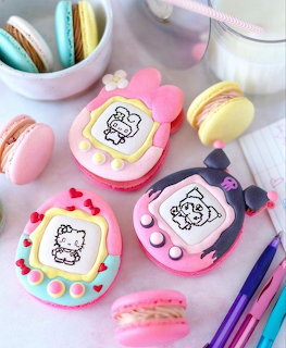 Macarons decorated to look like Tamagotchi devices with character screens and buttons, displayed with colorful macarons