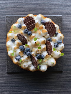 Overhead view of a dessert tart topped with golden meringue, blueberries, and chocolate wafers on slate