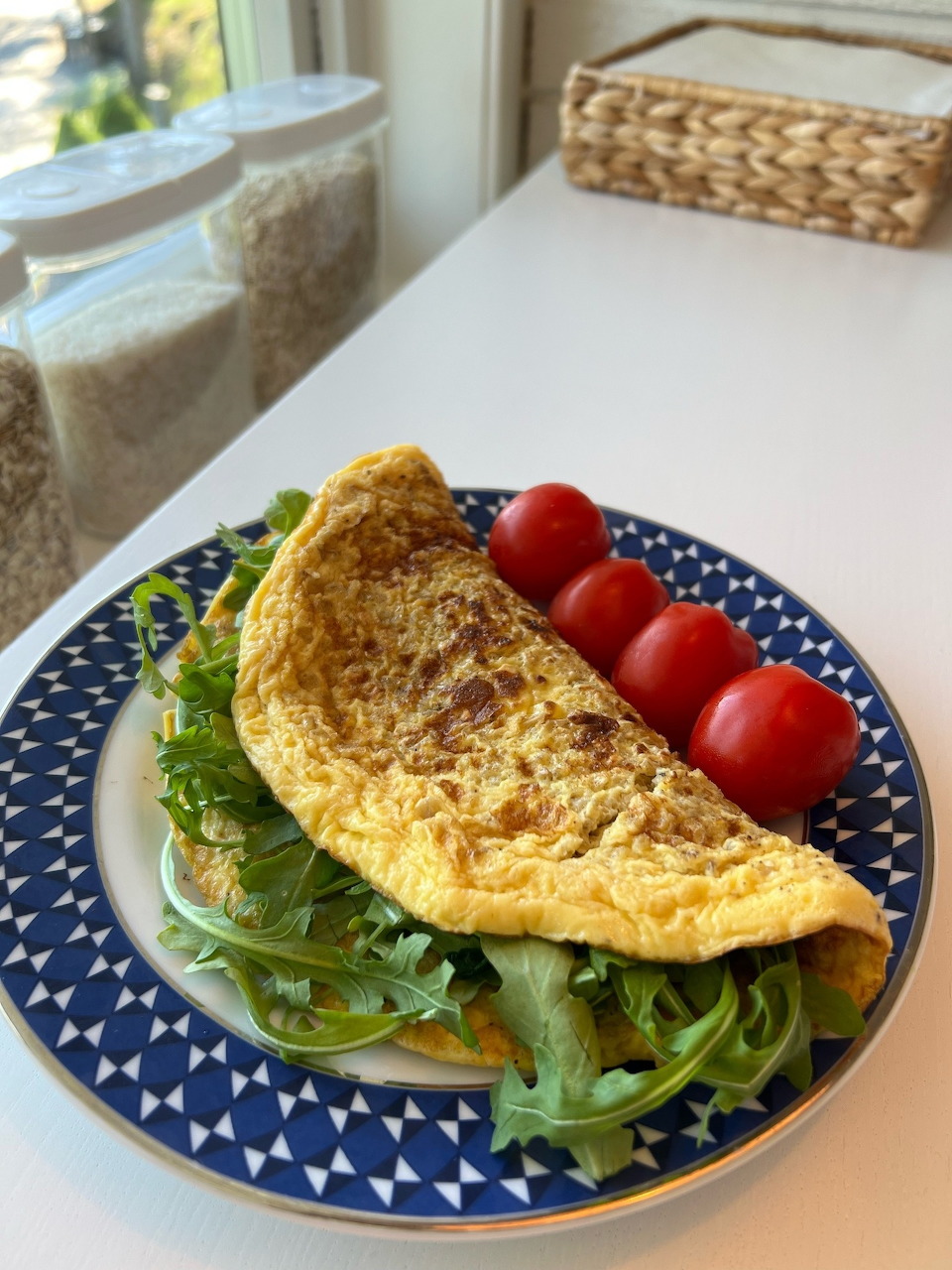 Folded egg omelet with arugula greens and cherry tomatoes on a blue patterned plate