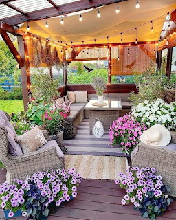 Covered patio decorated with wicker furniture, string lights, and vibrant purple and white flowers in planters