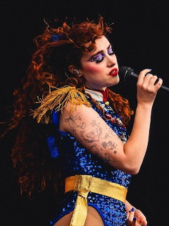 Chappell Roan singing into a microphone on stage in a blue sequined outfit