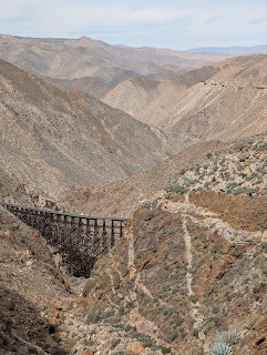 Wooden railroad trestle bridge crossing a deep desert canyon with rocky mountains in the background