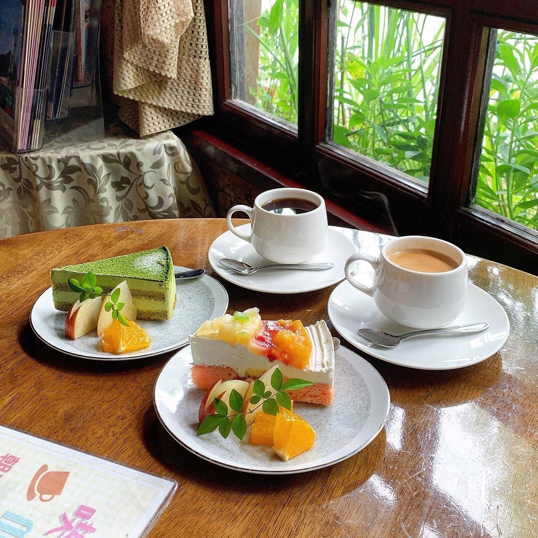 Two cups of coffee and slices of cake on a wooden table by a window