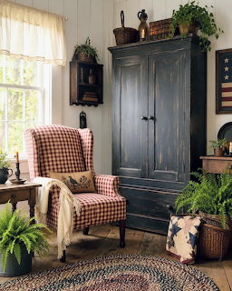 Primitive sitting room with dark armoire, checkered chair, plants, and rustic Americana decor