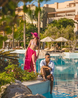 Couple posing by a tropical resort swimming pool with palm trees and greenery in the background