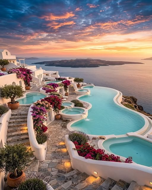 Terraced infinity pools with bougainvillea flowers overlooking the Aegean Sea at sunset in Santorini