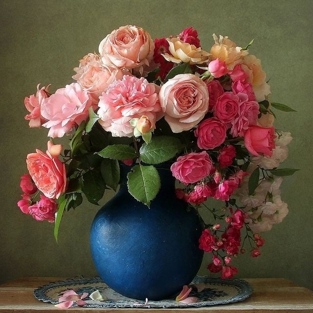 Still life painting of pink roses and mixed flowers in a blue vase on a table