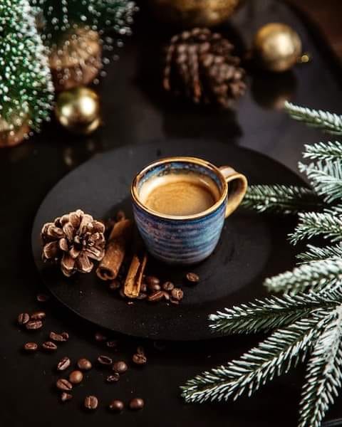 Blue cup of coffee on dark plate with pine cones, cinnamon sticks, coffee beans, and Christmas decorations
