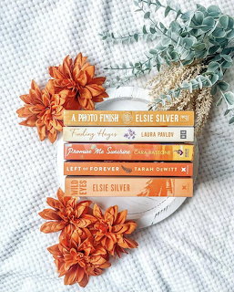 Stack of romance paperbacks with orange flowers and eucalyptus on white fabric