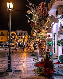 Nightime Greek island street decorated with Christmas lights, star ornaments, and red baubles