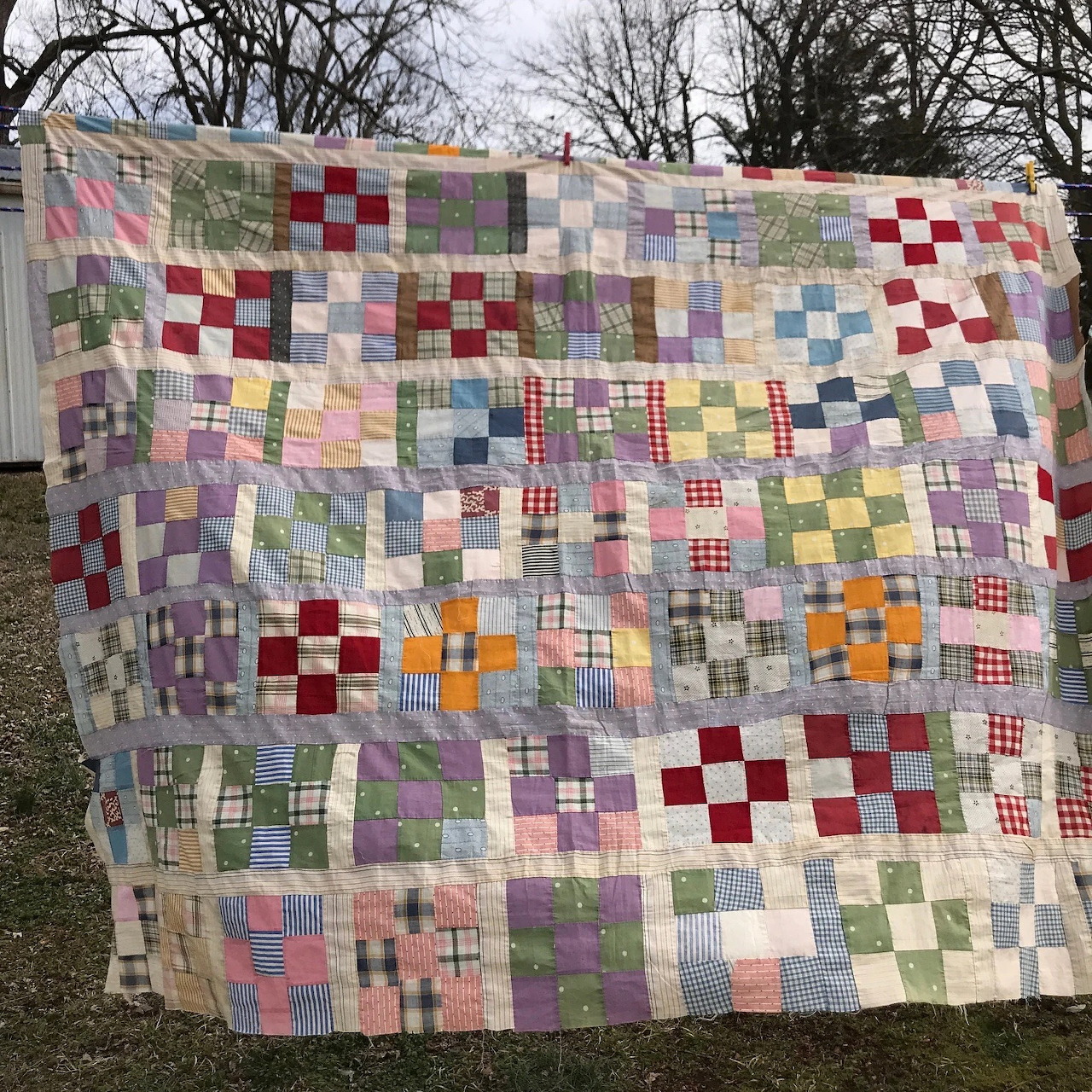 Handmade nine-patch quilt with multicolored fabric squares hung outdoors