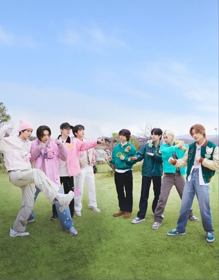 Eight young men posing together on grass under a blue sky in colorful casual clothes