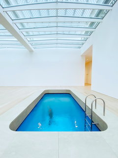 Minimalist indoor swimming pool beneath a large skylight with white walls and bright blue water