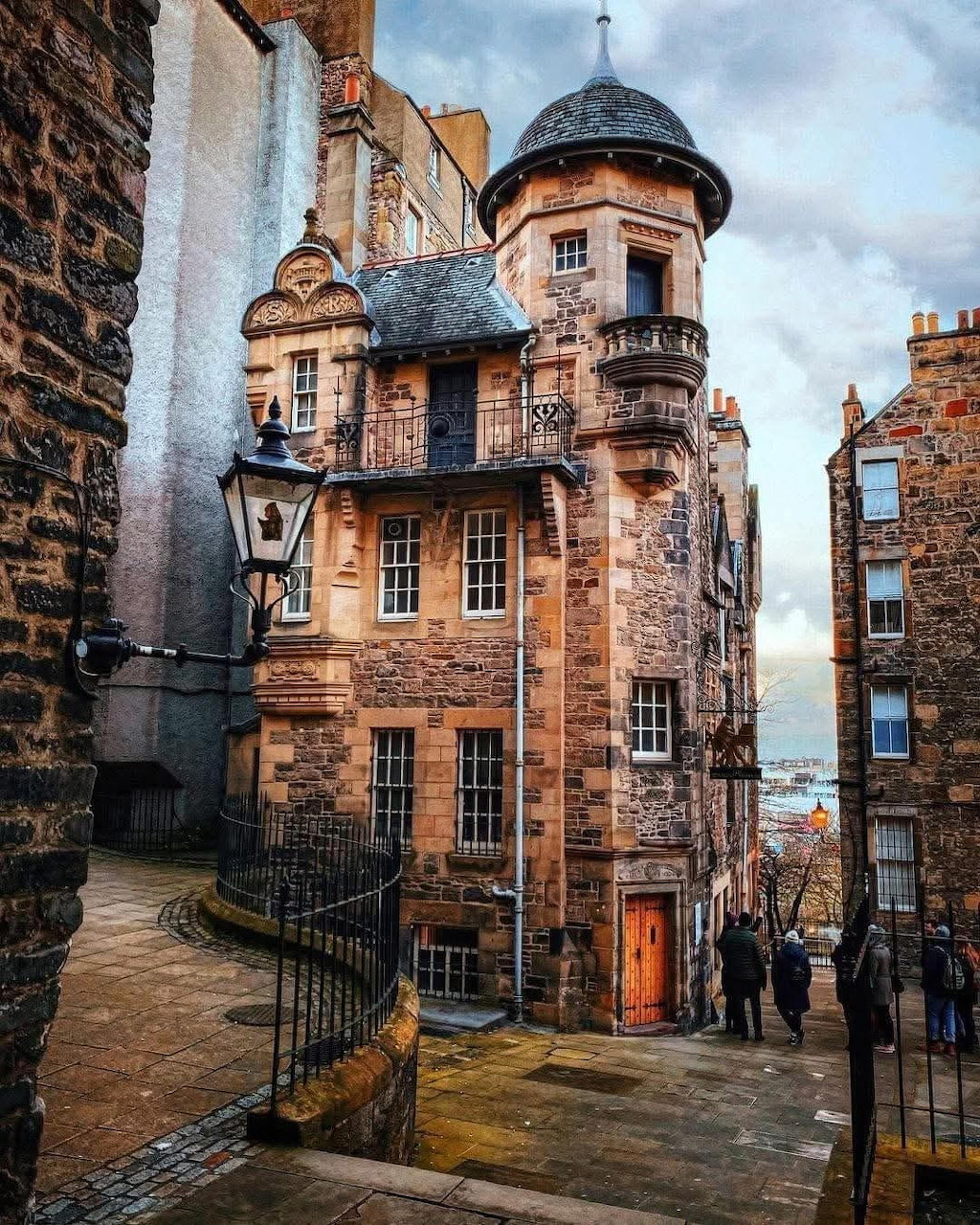 Historic stone building with turret in a narrow Edinburgh street with iron railings and old street lamp