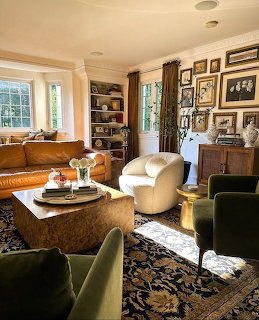 Elegant living room with leather sofa, cream armchair, green chairs, gallery wall, and patterned dark rug