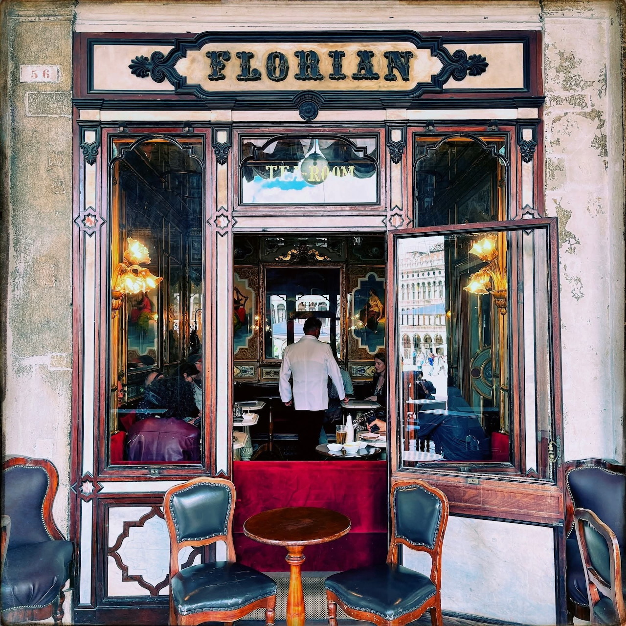Ornate cafe storefront with Florian sign, wooden frame, glass windows, and outdoor seating with red velvet chairs