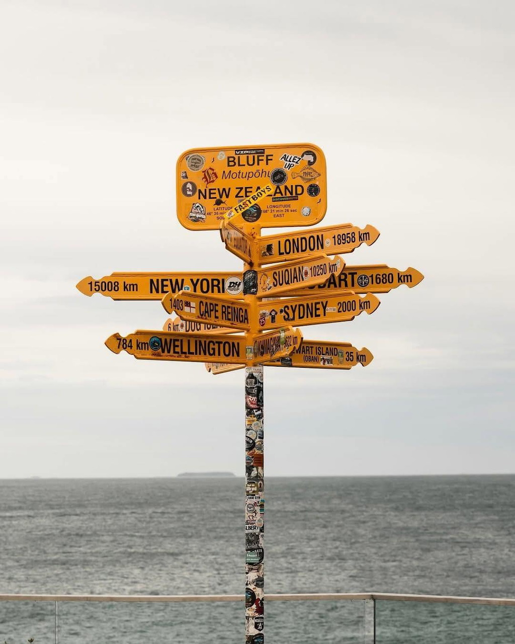 Yellow wooden signpost showing distances to world cities, ocean horizon behind, at Bluff New Zealand