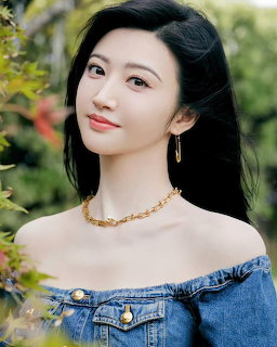Young Asian woman in off-shoulder denim jacket with gold chain necklace smiling outdoors