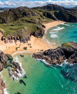 Aerial view of a sandy beach cove with rocky cliffs and turquoise water in Ireland