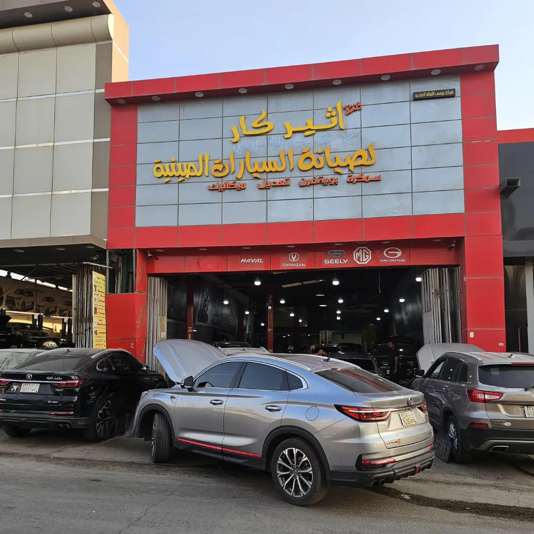 Car repair shop storefront with Arabic sign and three SUVs parked outside