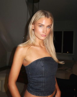 Blonde woman in dark denim strapless top posing indoors with warm lighting