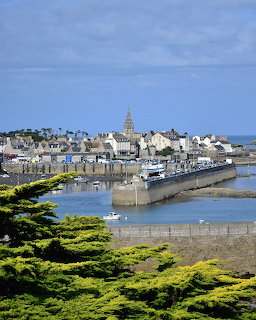 Coastal town of Roscoff with harbour, stone buildings, church spire, boats, and green trees