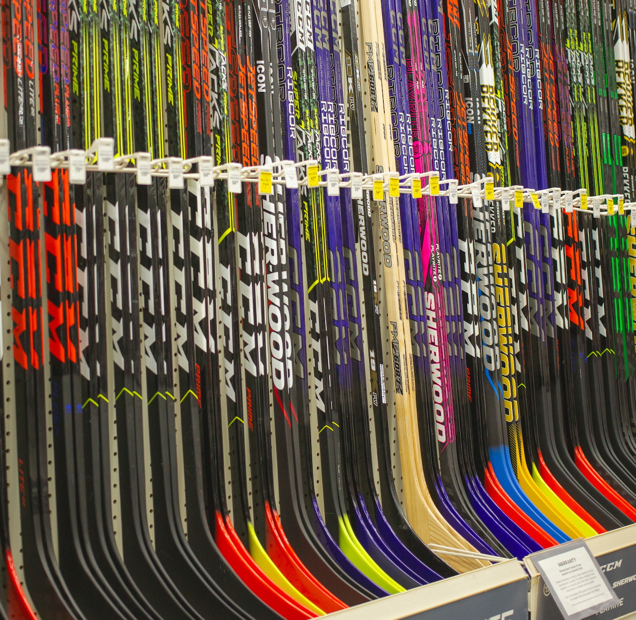 Colorful hockey sticks arranged upright in a store rack with curved blades at the bottom