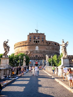 Castel Sant’Angelo in Rome seen from the bridge with statues and people walking toward the fortress