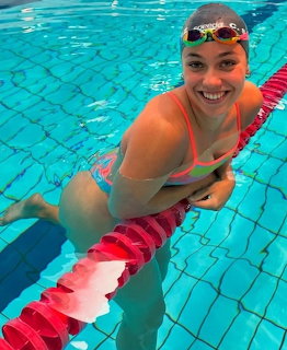 Smiling woman swimmer in colorful swimsuit posing in a turquoise pool with goggles and swim cap