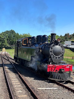 Black vintage steam train with red accents on tracks emitting smoke under blue sky
