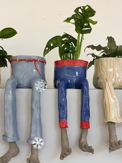 Four ceramic leg-shaped planters wearing colorful pants, holding tropical plants on a white shelf.