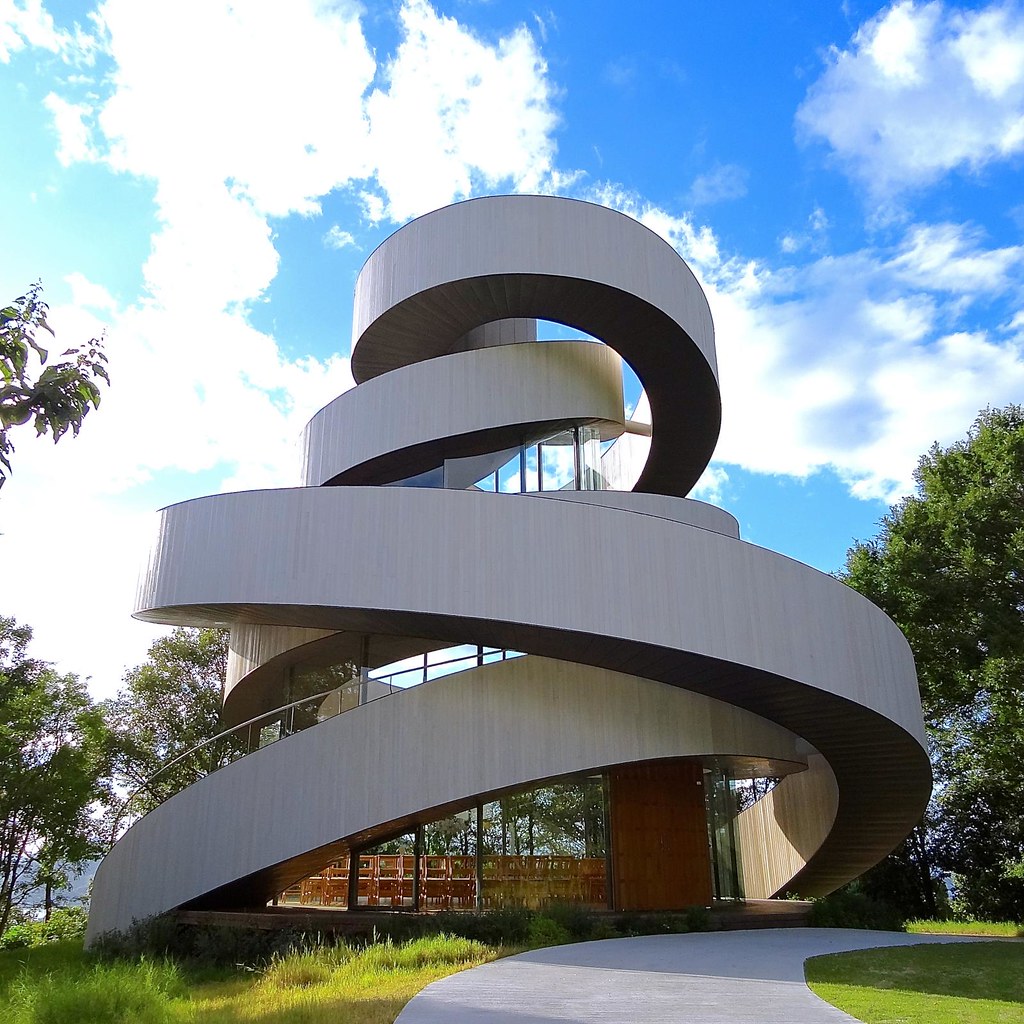 Modern spiral-shaped white building on a grassy lawn beneath a blue sky with clouds