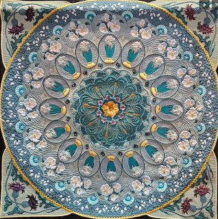 Ornate circular quilt with symmetrical floral mandala pattern in teal, cream and gold tones