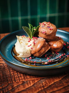 Stack of three glazed donuts with vanilla ice cream scoop, mint leaves, and sprinkles on a teal plate