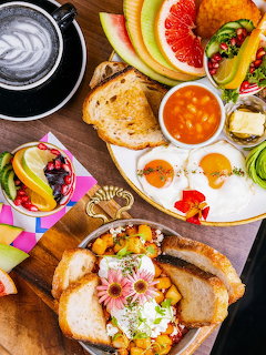 Overhead breakfast spread with eggs, toast, fruit, coffee and pastries on wooden table