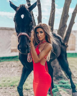 Woman in red dress standing beside black horse in outdoor setting