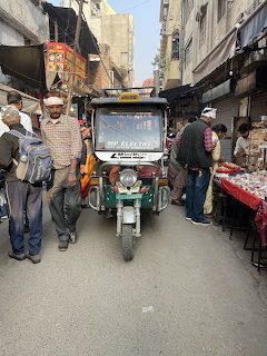 Green electric rickshaw on a narrow Indian market street with people and shops
