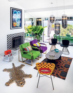 Modern living room with green chairs, purple ottoman, black wire furniture, patterned rugs, and geometric fireplace