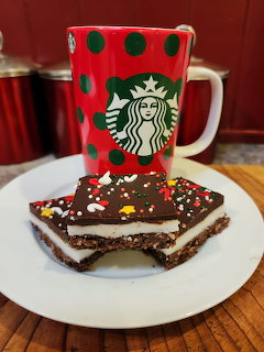 Red polka dot coffee mug beside chocolate peppermint layered dessert bar with sprinkles on white plate