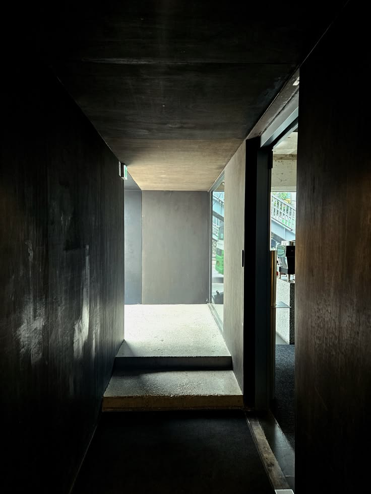 Dark hallway with dark wood walls and concrete ceiling leading to a bright cafe entrance