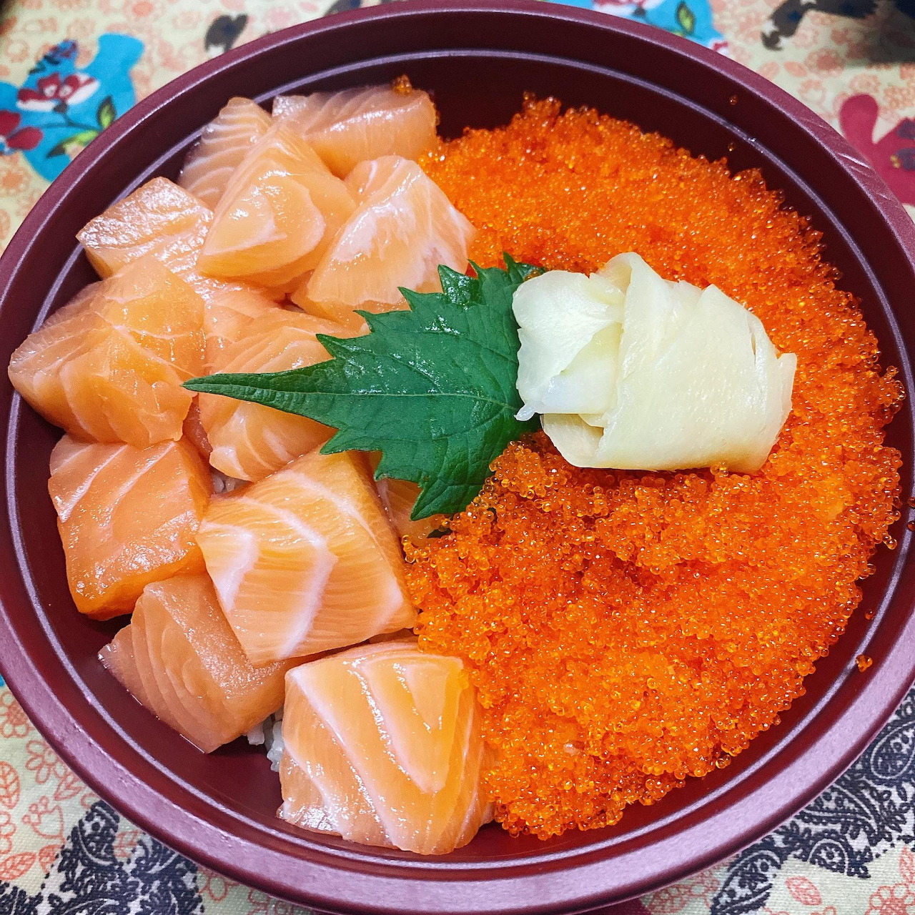 Rice bowl with salmon sashimi, orange fish roe, shiso leaf and wasabi in dark bowl