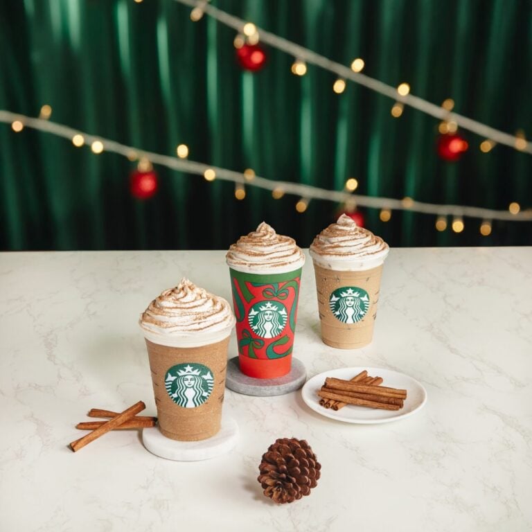 Three Starbucks holiday lattes with whipped cream, cinnamon sticks, and Christmas decorations