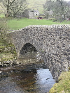 Old stone arch bridge over a shallow stream in a rural grassy landscape