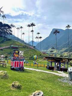 Tall wax palms in Cocora Valley, Colombia, with green hills, mountains, and small colorful huts