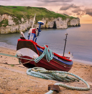 Red and blue fishing boat on beach with white cliffs and sea arch at sunset