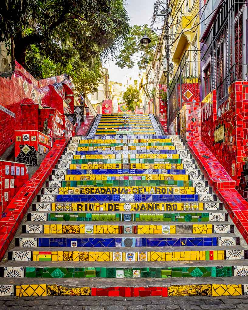Vibrant mosaic staircase with colorful tiles in Rio de Janeiro, surrounded by red buildings and greenery
