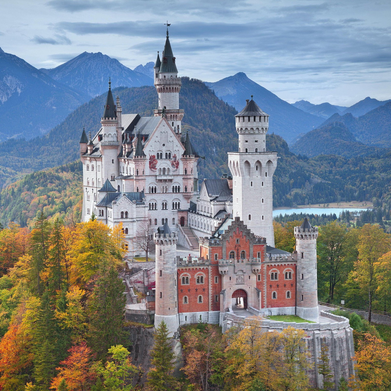 Neuschwanstein Castle with white towers against mountains and autumn foliage